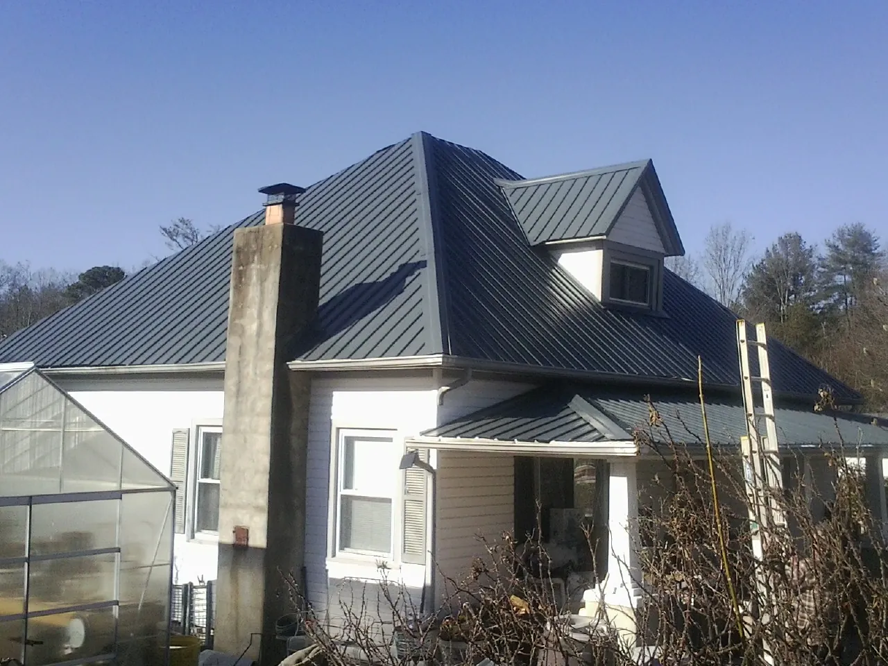 Dark blue standing seam metal roof on a white farmhouse with dormer — Slate & Tile Roof Repair by Roofing Brothers in Seaview