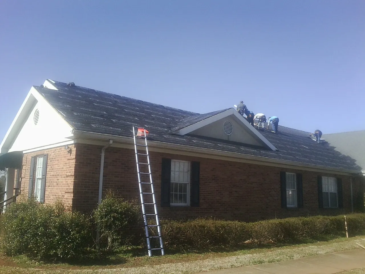 Crew tearing shingles off a brick ranch roof with a ladder set — Emergency Roof Repair work by our crew in Seaview