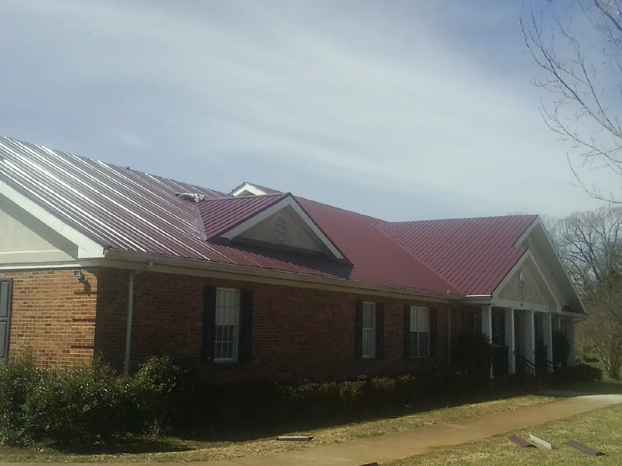 Red metal roof with gabled entries on a long brick building, from a Hail Damage Roof Repair job in Seaview