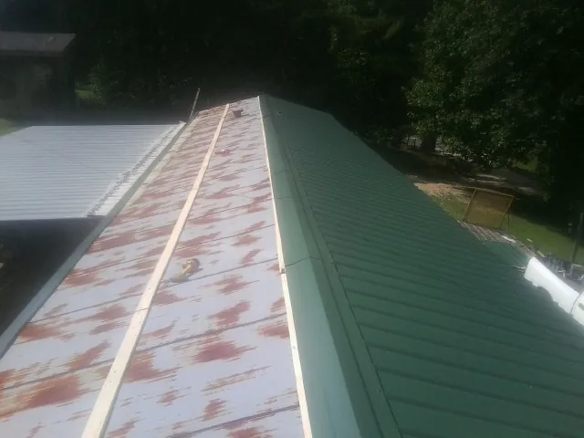 Old rusted panels beside newly installed green metal roofing — Wind Damage Roof Repair by Roofing Brothers in Seaview