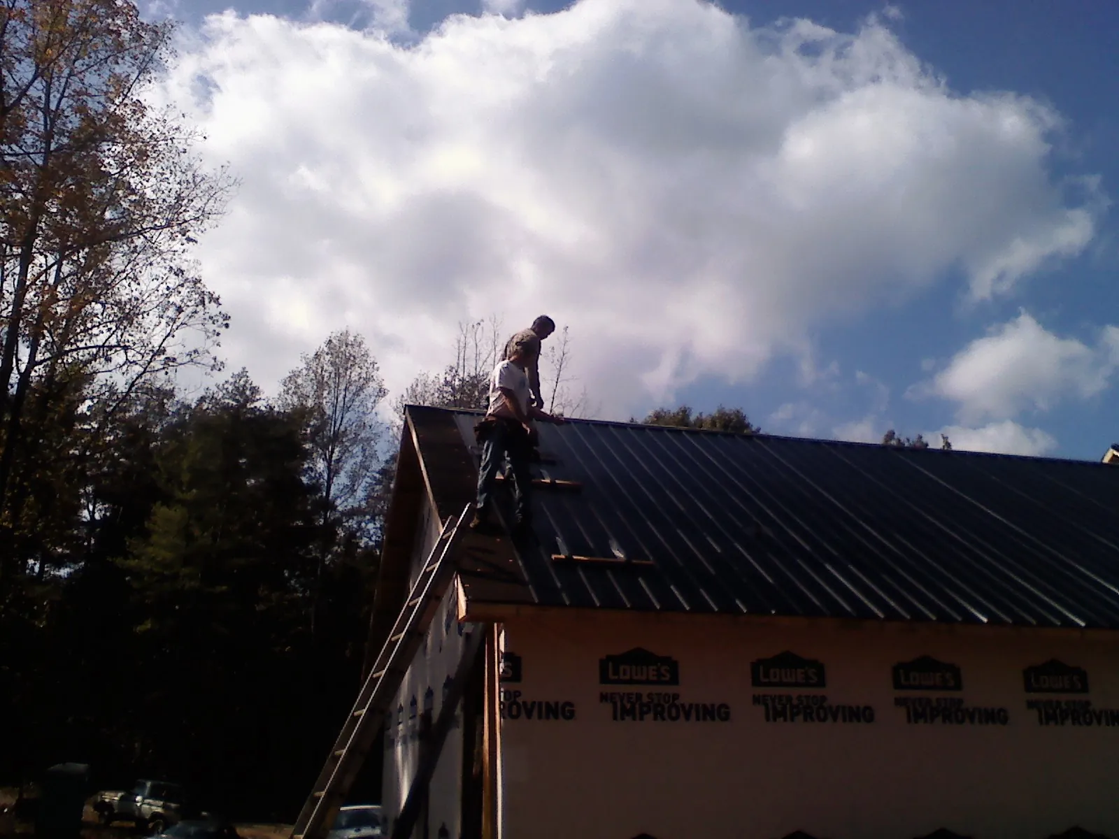 Roofer fastening dark metal panels high against a cloudy sky, from a Roof Inspection job in Seaview