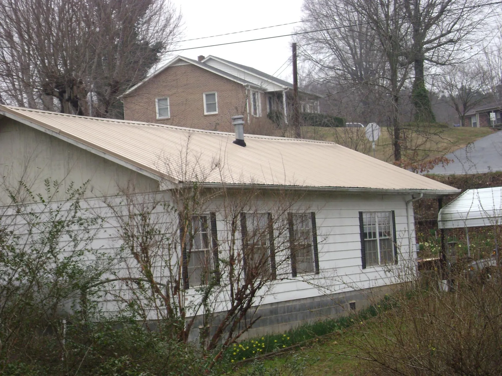 Tan metal roof on a white sided house set into a hillside — Commercial Roofing by Roofing Brothers in Seaview